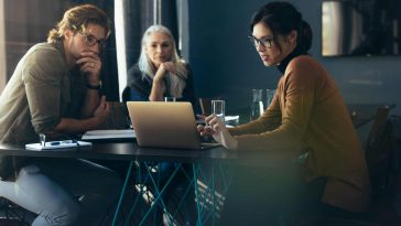 three people sitting at a table looking at a presentation on a computer